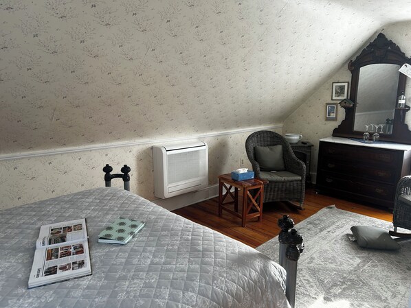 A bedroom with a bed, a chair, a dresser, a radiator, and a mirror.