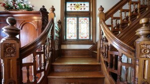 Una escalera de madera con barandillas ornamentales y un ventanal de vitral en la parte superior.