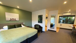 A modern hotel room with a large bed, a seating area, and a view of the outdoors. - Commodore Motels (Dunedin)