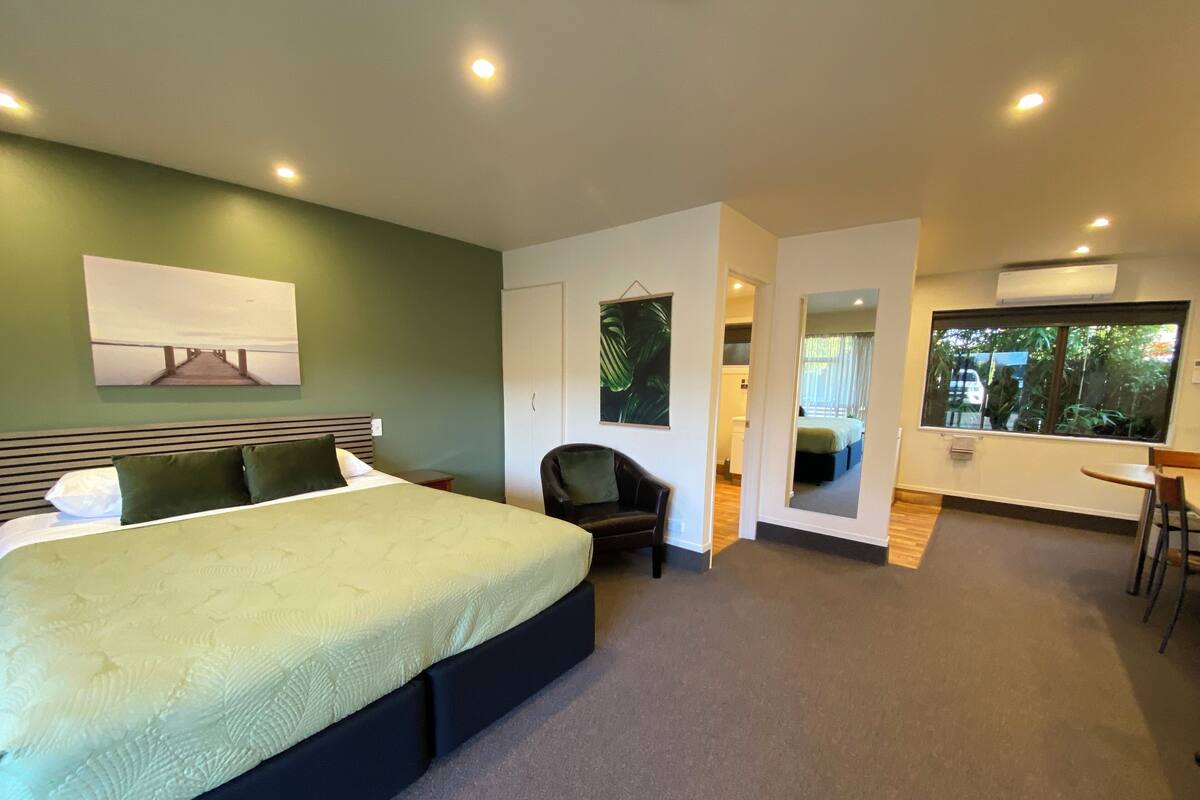 A modern hotel room with a large bed, a seating area, and a view of the outdoors.
