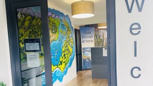 A reception area with a large welcome sign, a world map mural, and a wooden floor. - Commodore Motels (Dunedin)
