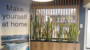 A reception desk with a sign that reads 'Make yourself at home,' a lamp, a remote control, and a plant arrangement. - Commodore Motels (Dunedin)
