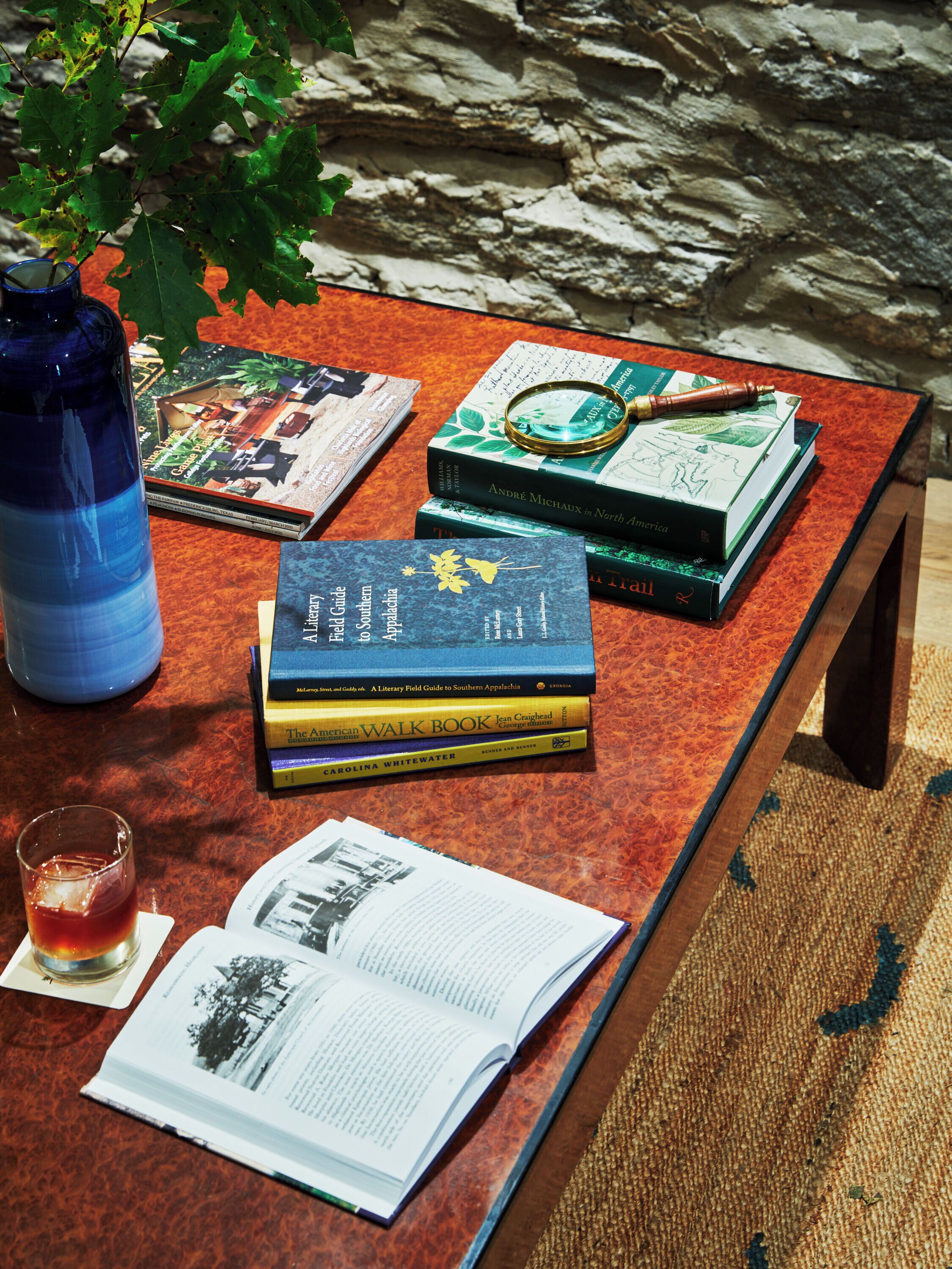 A table with books, a magnifying glass, a pen, and a glass of drink.