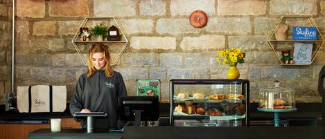 A coffee shop counter with a cash register, a display case with pastries, and a clock on the wall.