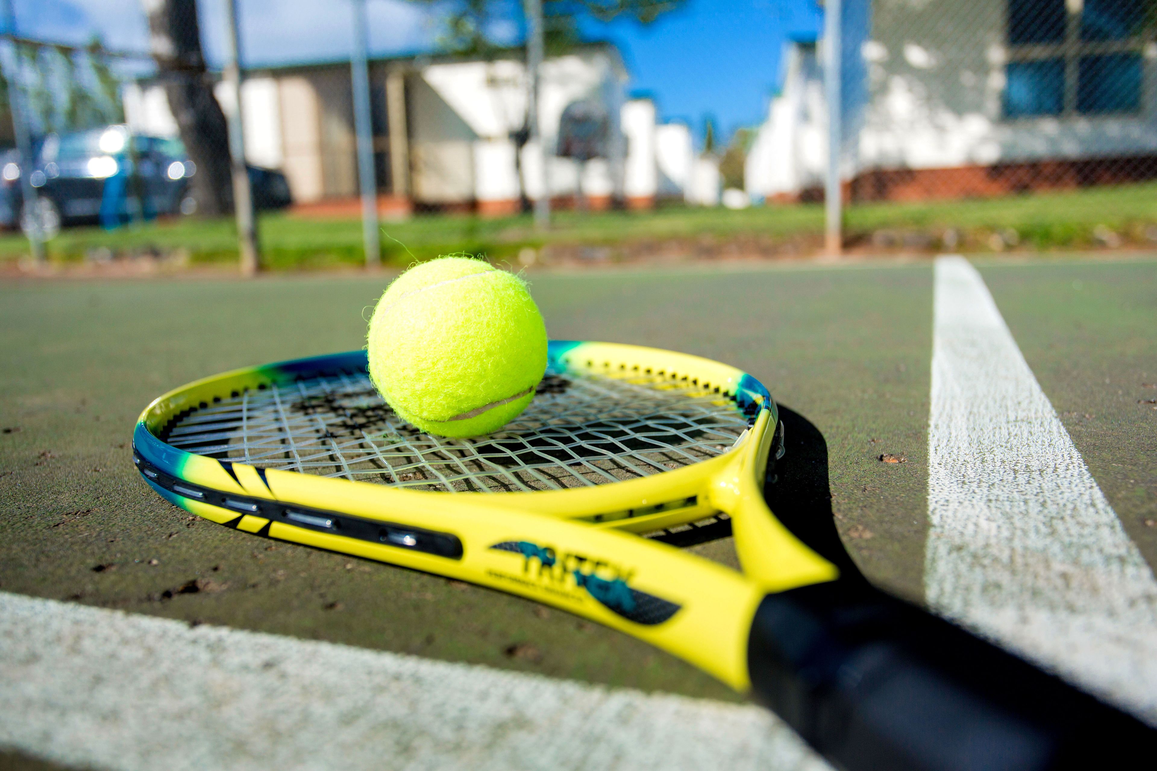 A tennis racket with a yellow grip and a tennis ball on a court.
