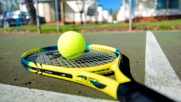 Una raqueta de tenis con empuñadura amarilla y una pelota de tenis en la cancha.