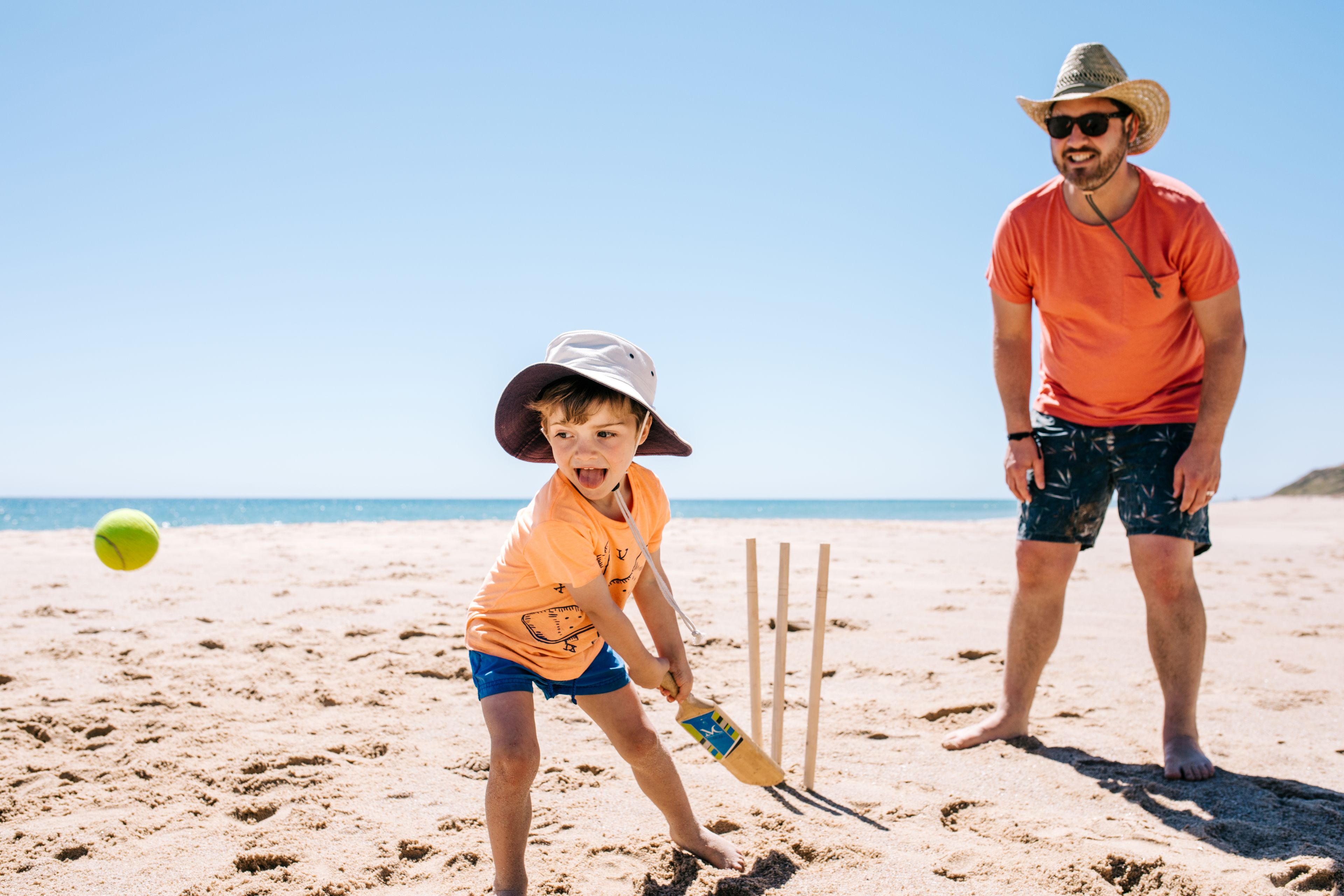 Une plage de sable où une personne joue au cricket et une autre se tient à proximité.
