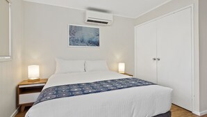A neatly made bed with a patterned blanket, a bedside lamp, and an air conditioning unit on the wall. - Discovery Parks - Coogee Beach (Coogee)