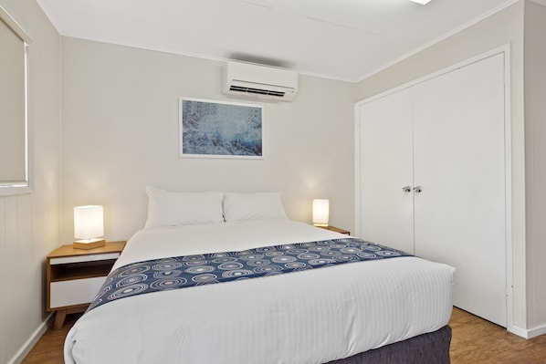 A neatly made bed with a patterned blanket, a bedside lamp, and an air conditioning unit on the wall.