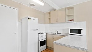 A modern kitchen with white appliances, a granite countertop, and beige cabinetry. - Discovery Parks - Coogee Beach (Coogee)