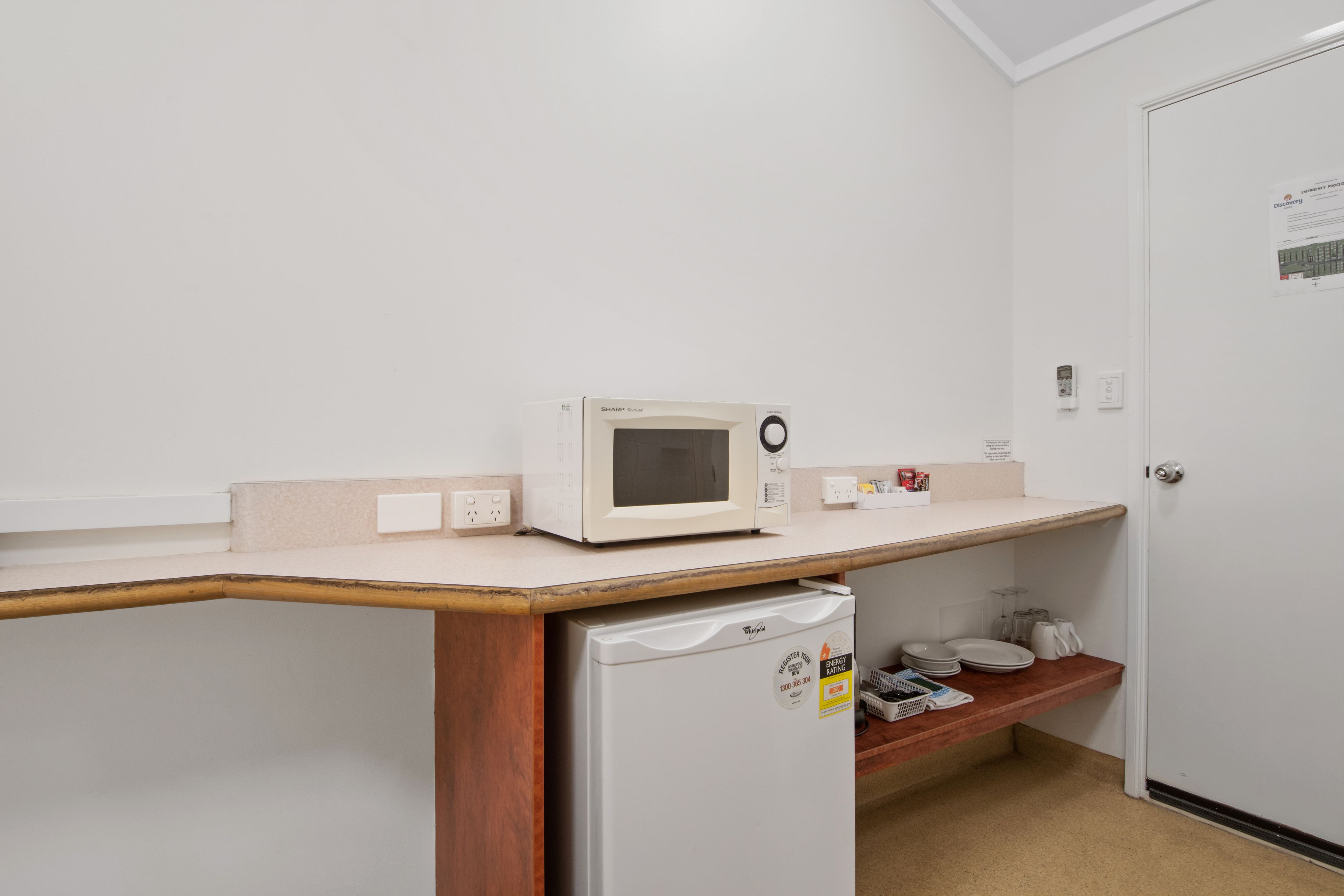 A kitchenette with a microwave, refrigerator, and a small shelf with dishes.