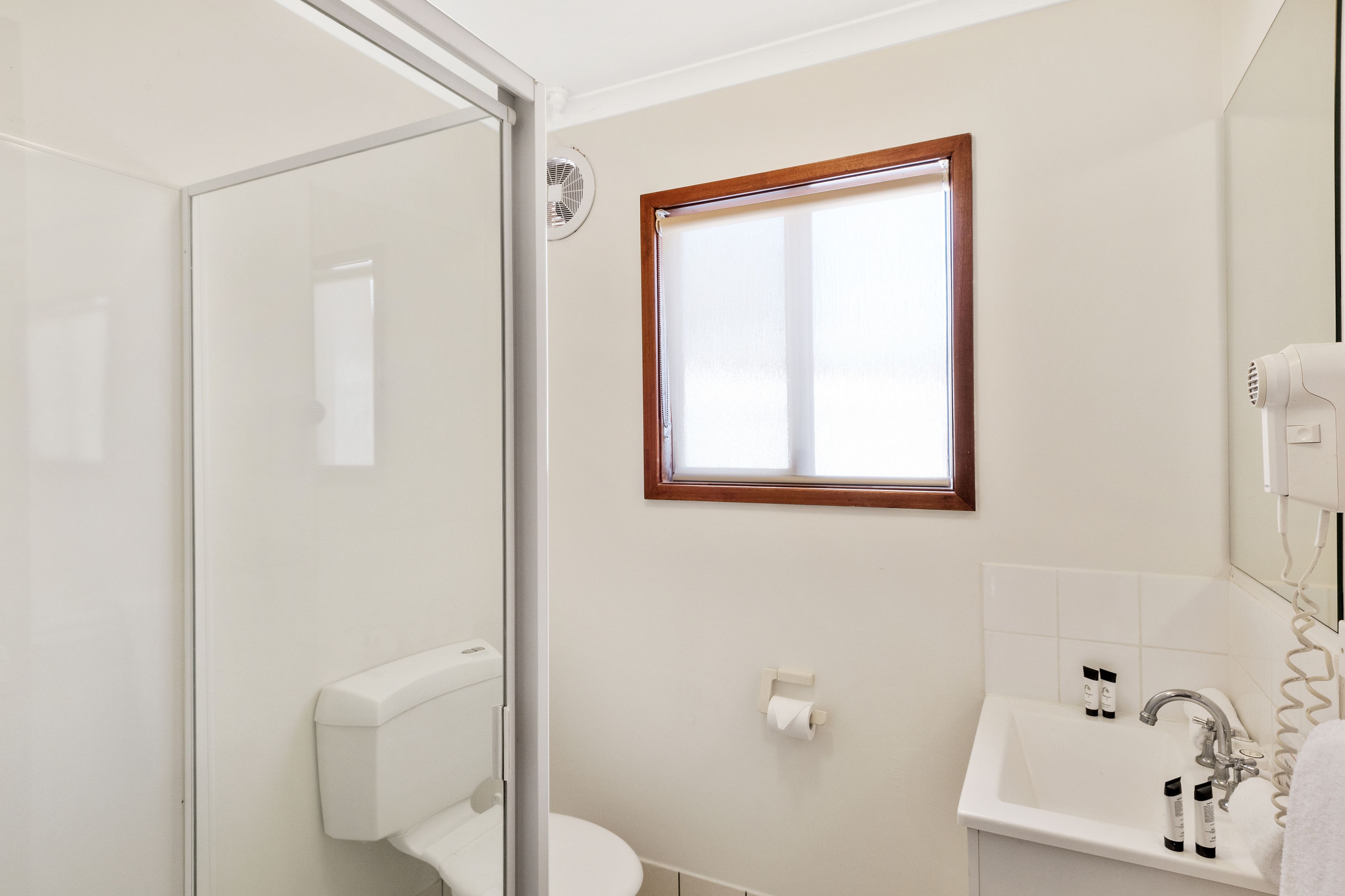 Un bagno con cabina doccia in vetro, un water, un lavabo con articoli da toilette e una finestra con stipite in legno.