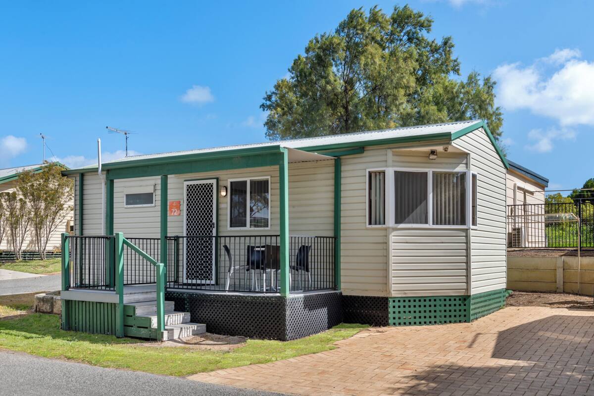 Ein Mobilheim mit Veranda, kleiner Terrasse und umzäunter Fläche.