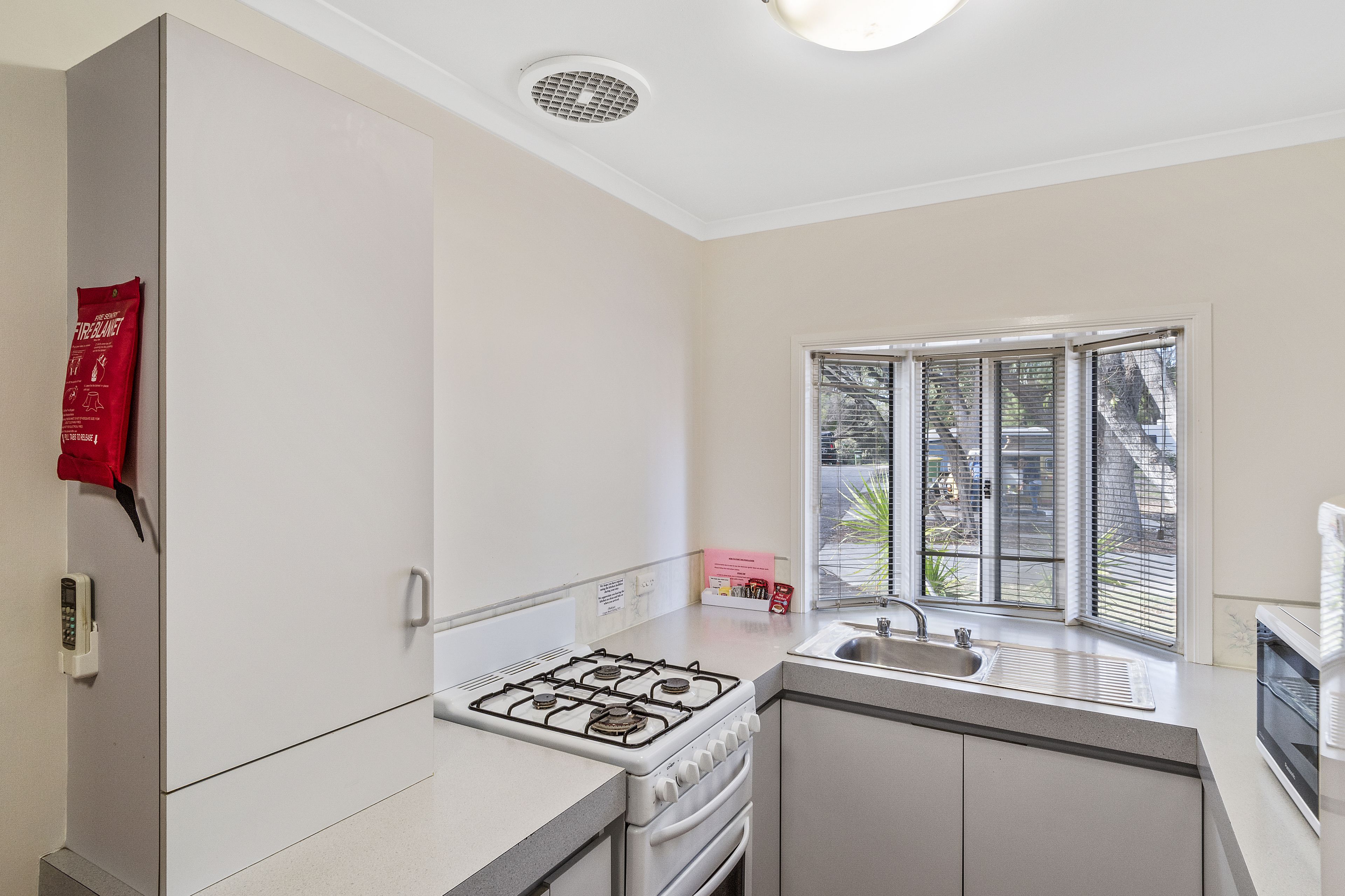 A modern kitchen with a gas stove, a built-in oven, a sink, and a window with blinds.
