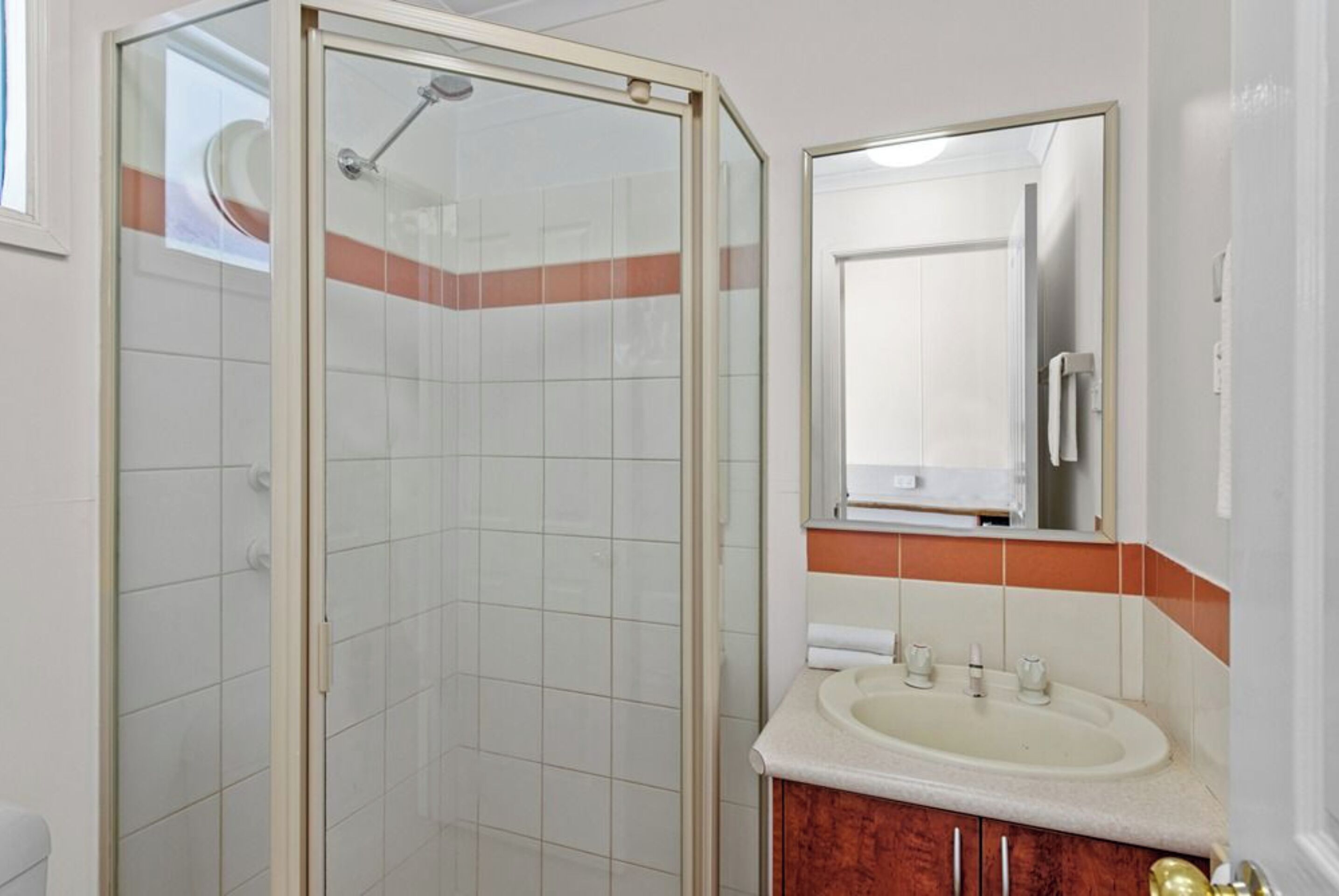 A bathroom with a glass shower enclosure, a sink, and a mirror.