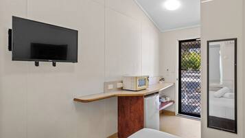 Habitación de hotel compacta con televisión de pantalla plana en la pared, una kitchenette pequeña con microondas, y una cama con vistas al exterior.