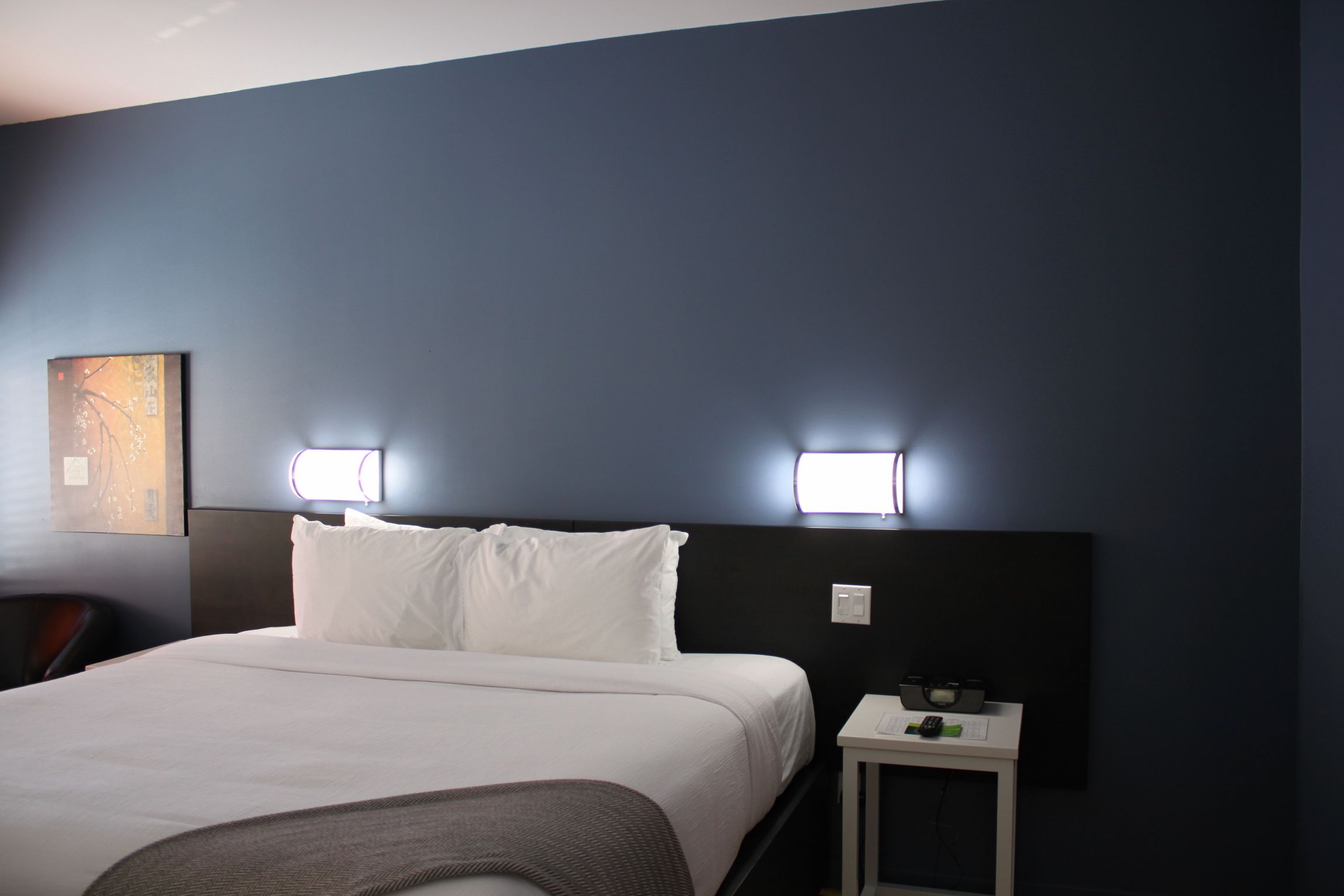 A hotel room with a large bed, two bedside lamps, a small table with a remote control, and a chair.
