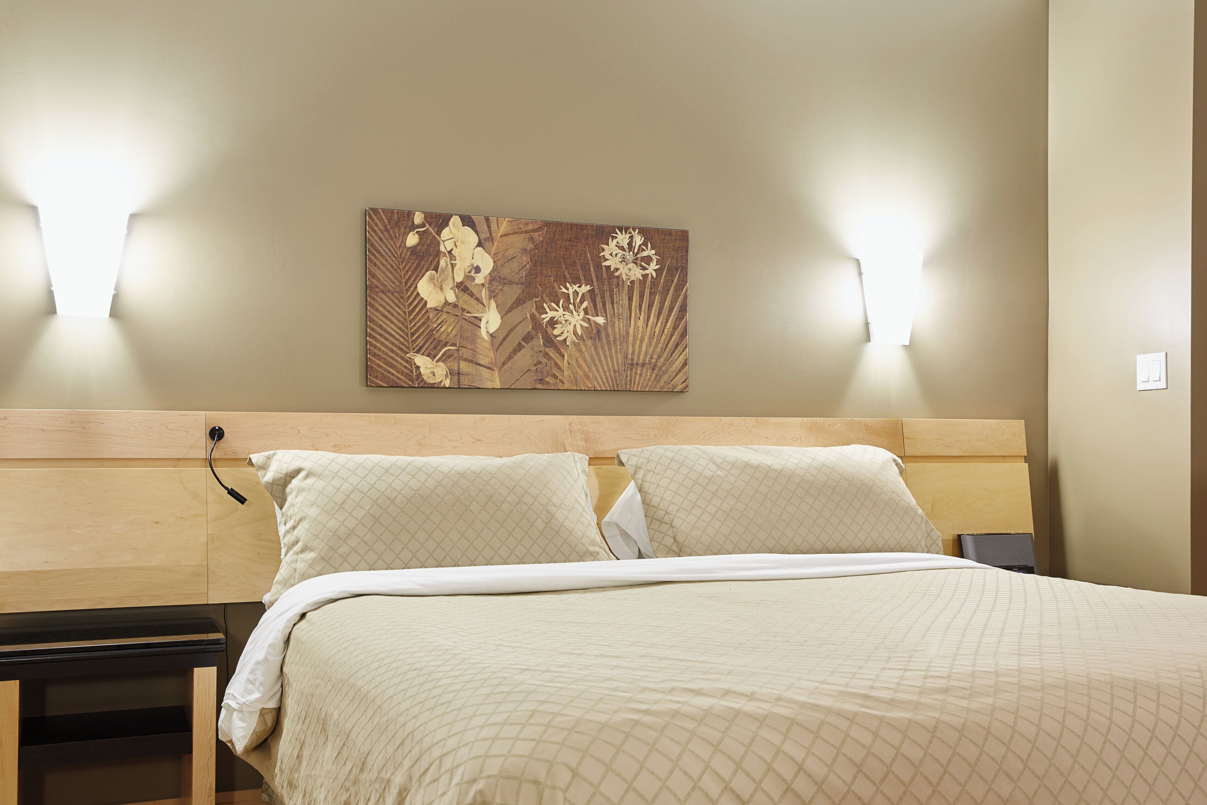 Cama bem arrumada com cabeceira, duas mesas de cabeceira e uma obra de arte na parede.