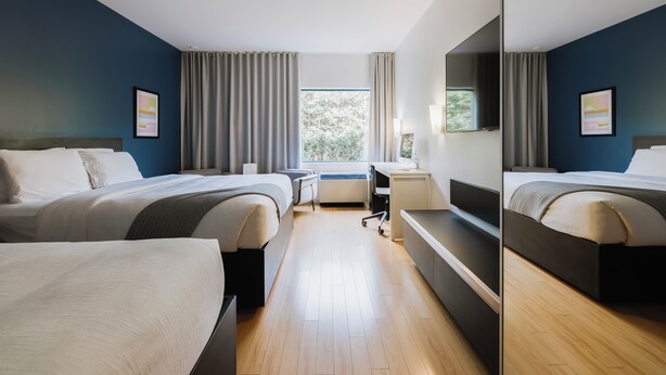 A modern hotel room with two beds, a desk, and a large window. - Hôtel Le Dauphin Saint-Hyacinthe (Saint Hyacinthe)