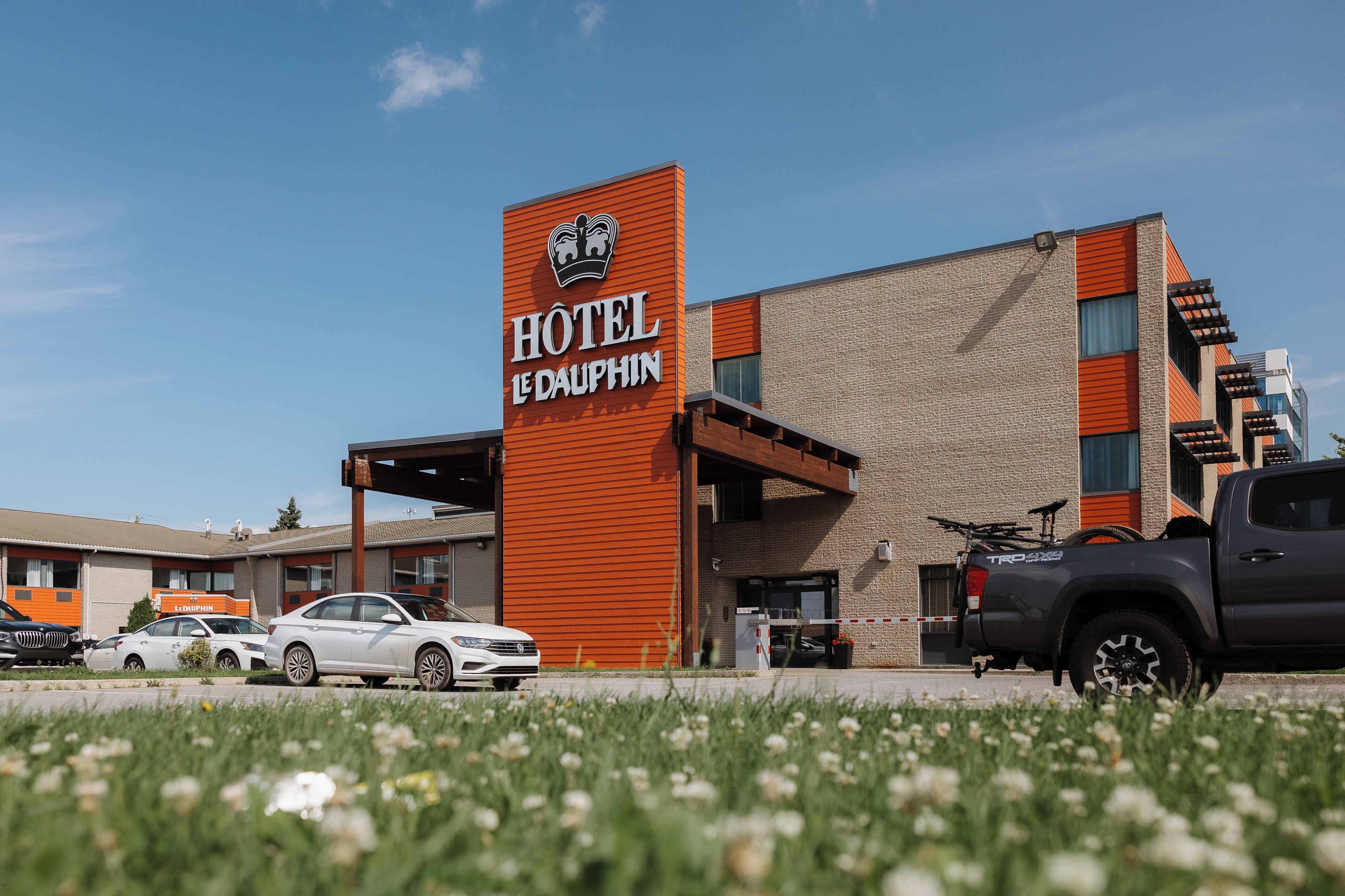 Un hotel con un letrero llamativo, un estacionamiento con varios autos y un cielo azul despejado.