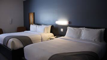 A hotel room with two beds, a nightstand, a wall-mounted lamp, and a painting.