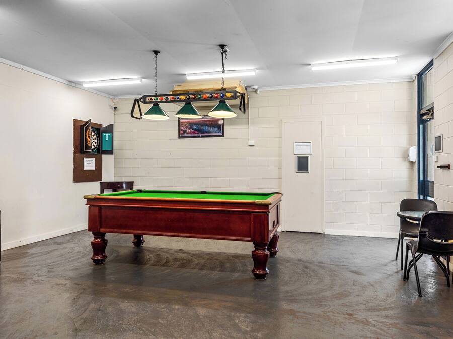 A pool table in a room with a brick wall, a door, and two chairs.