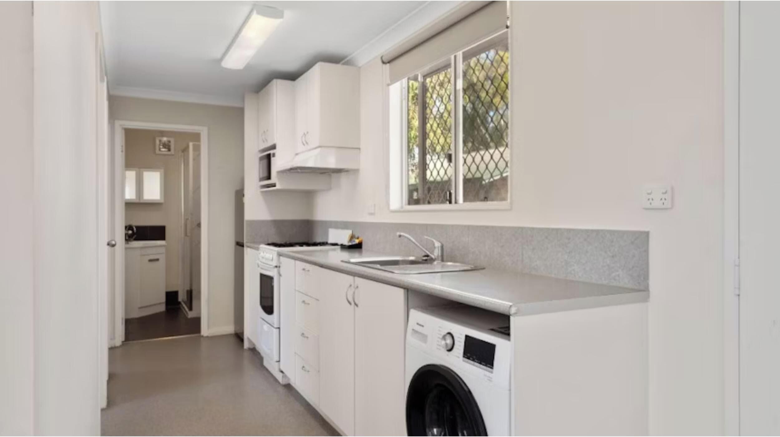 A compact kitchen with a washing machine, a stove, and a microwave.