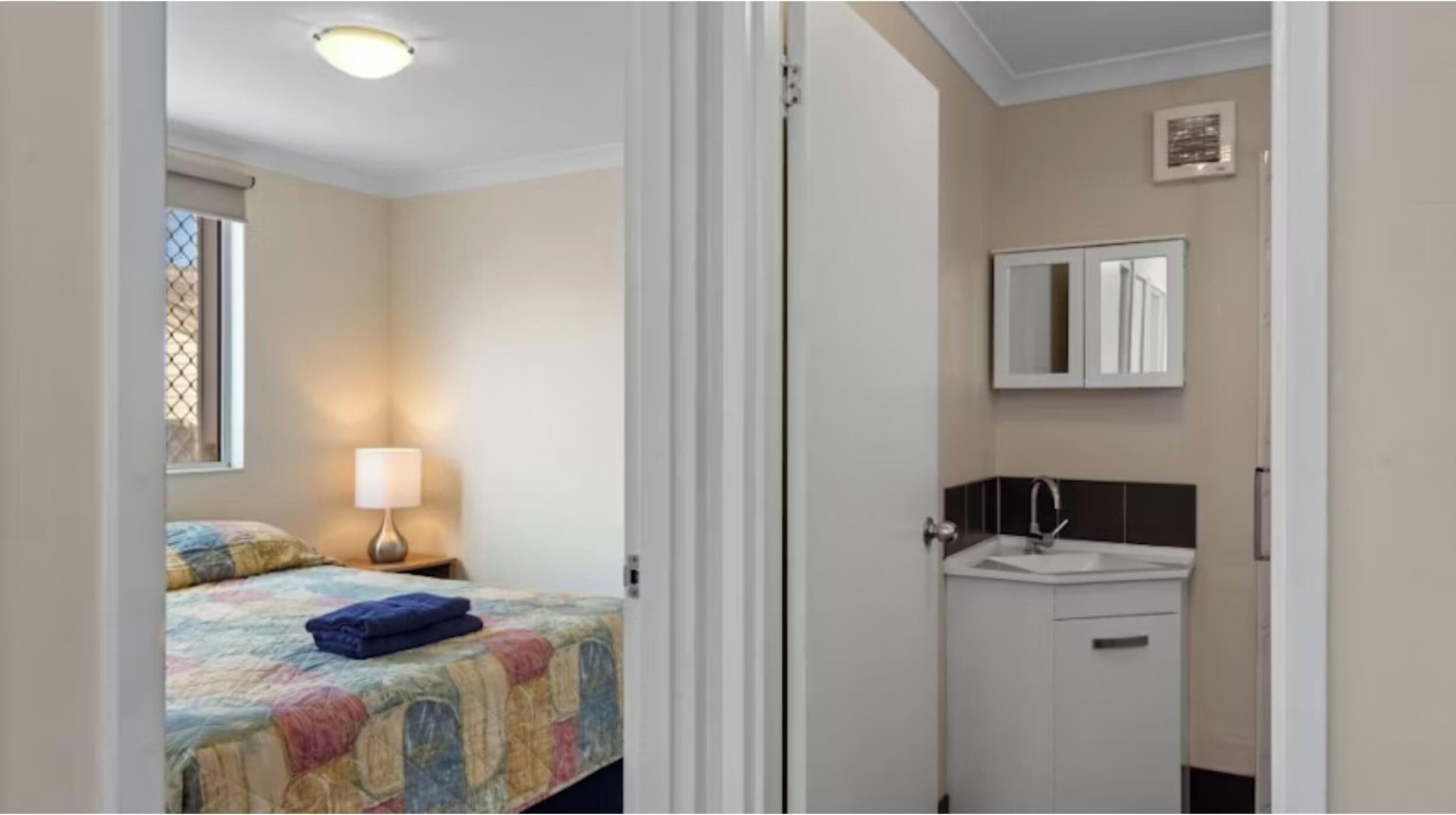 Un dormitorio con cama, lámpara de noche y ventana.