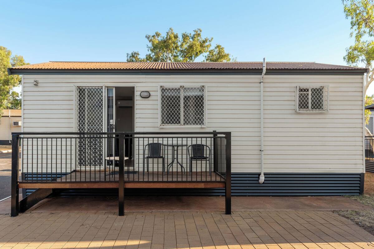 A single-story mobile home with a fenced porch, two chairs, and a small table.
