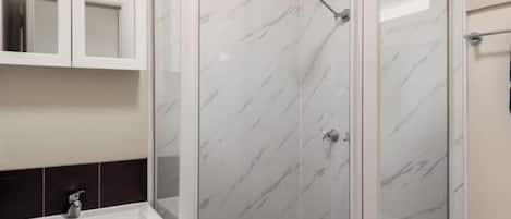 Un baño con cabina de ducha de mármol blanco, un lavabo blanco y un espejo sobre el lavabo.