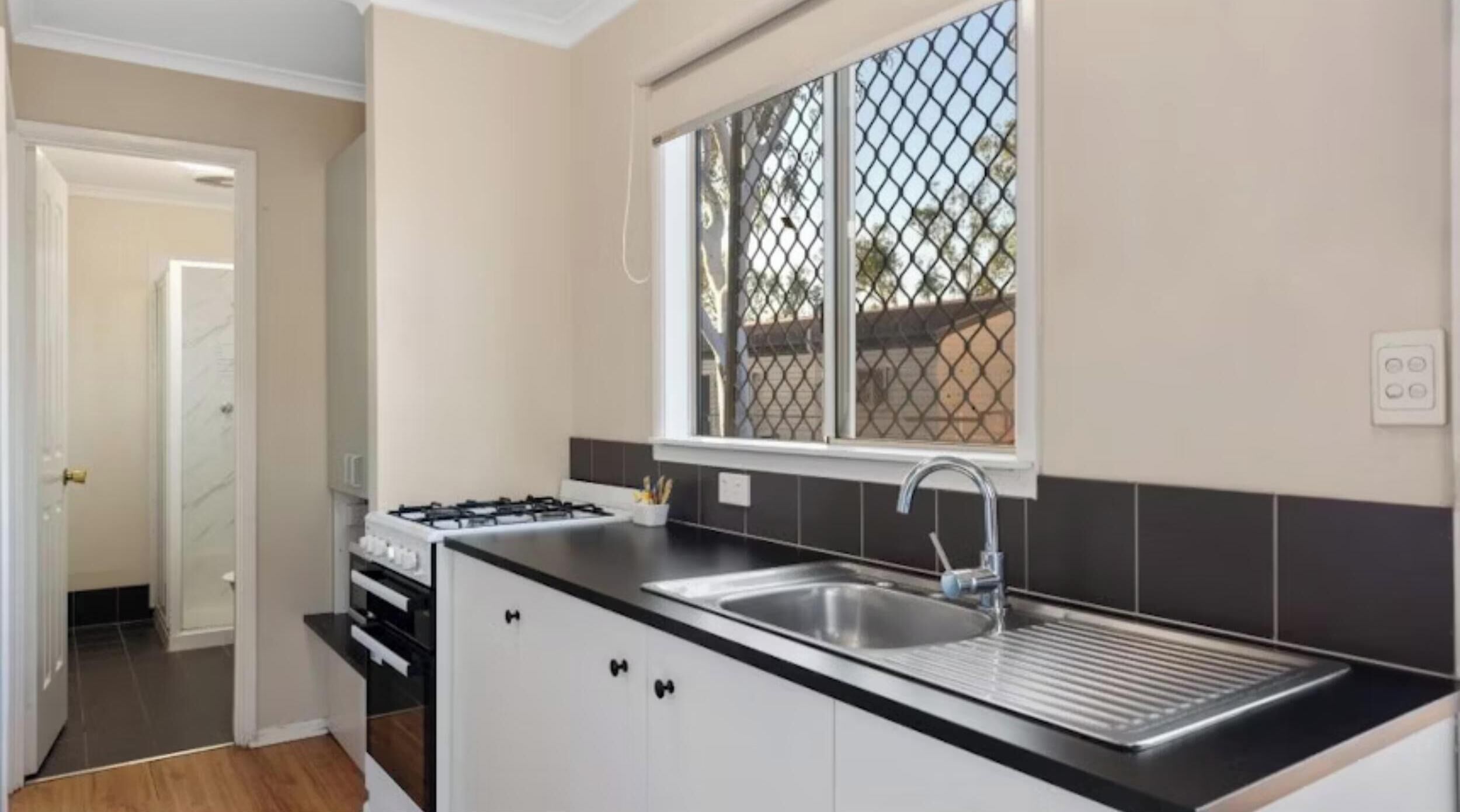 A modern kitchen with a gas stove, stainless steel sink, and a window with a metal screen.