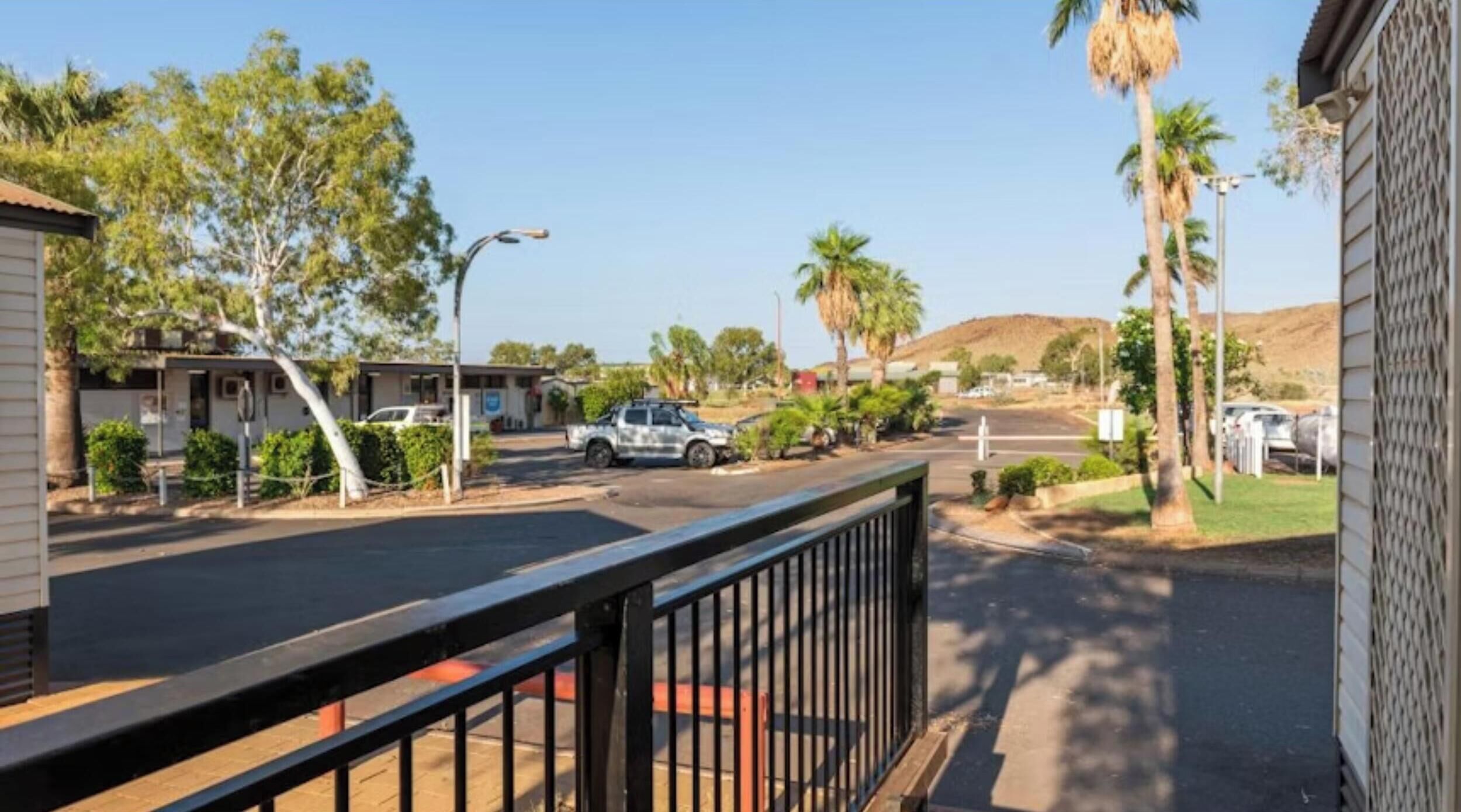 Et gadesyn med en bygning til venstre, en parkeret bil og palmer.