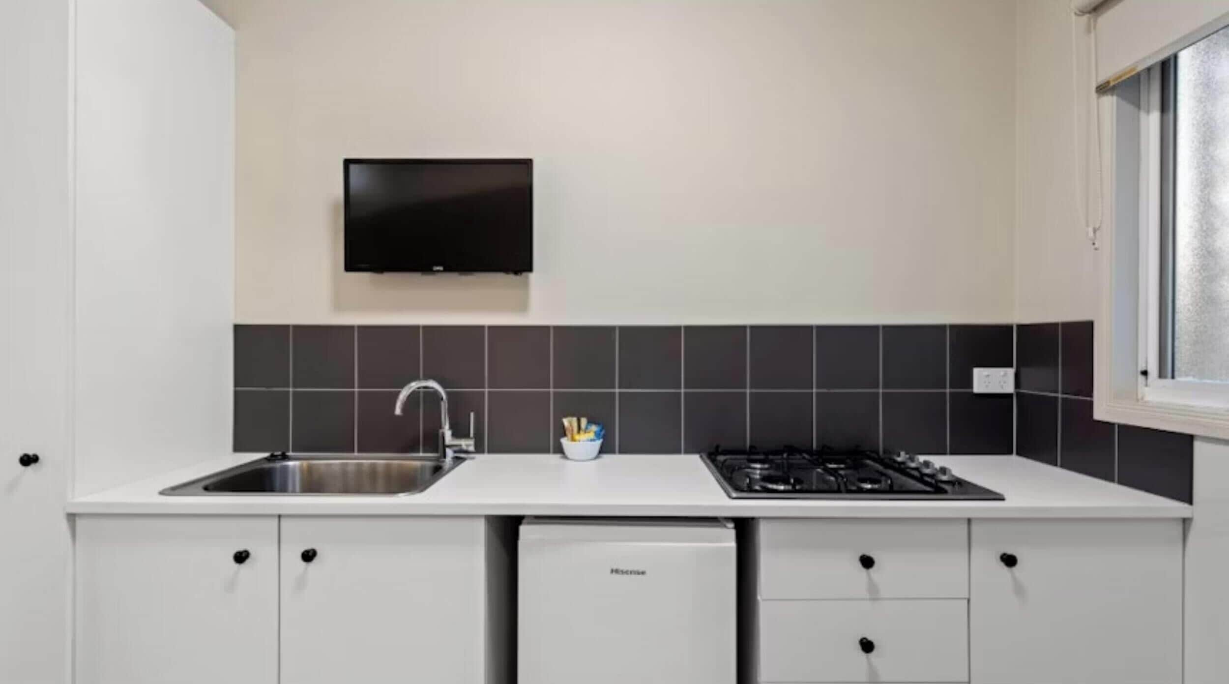 A modern kitchen with a built-in dishwasher, a gas stove, and a flat-screen TV mounted above the sink.
