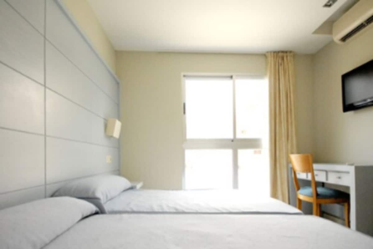 A hotel room with two beds, a desk, a chair, and a TV.