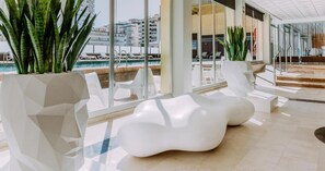 A modern indoor pool area with white lounge chairs and large potted plants. - Hotel Safari (Gandia)