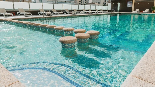 A swimming pool with clear blue water, lounge chairs, and a tiled deck. - Hotel Safari (Gandia)