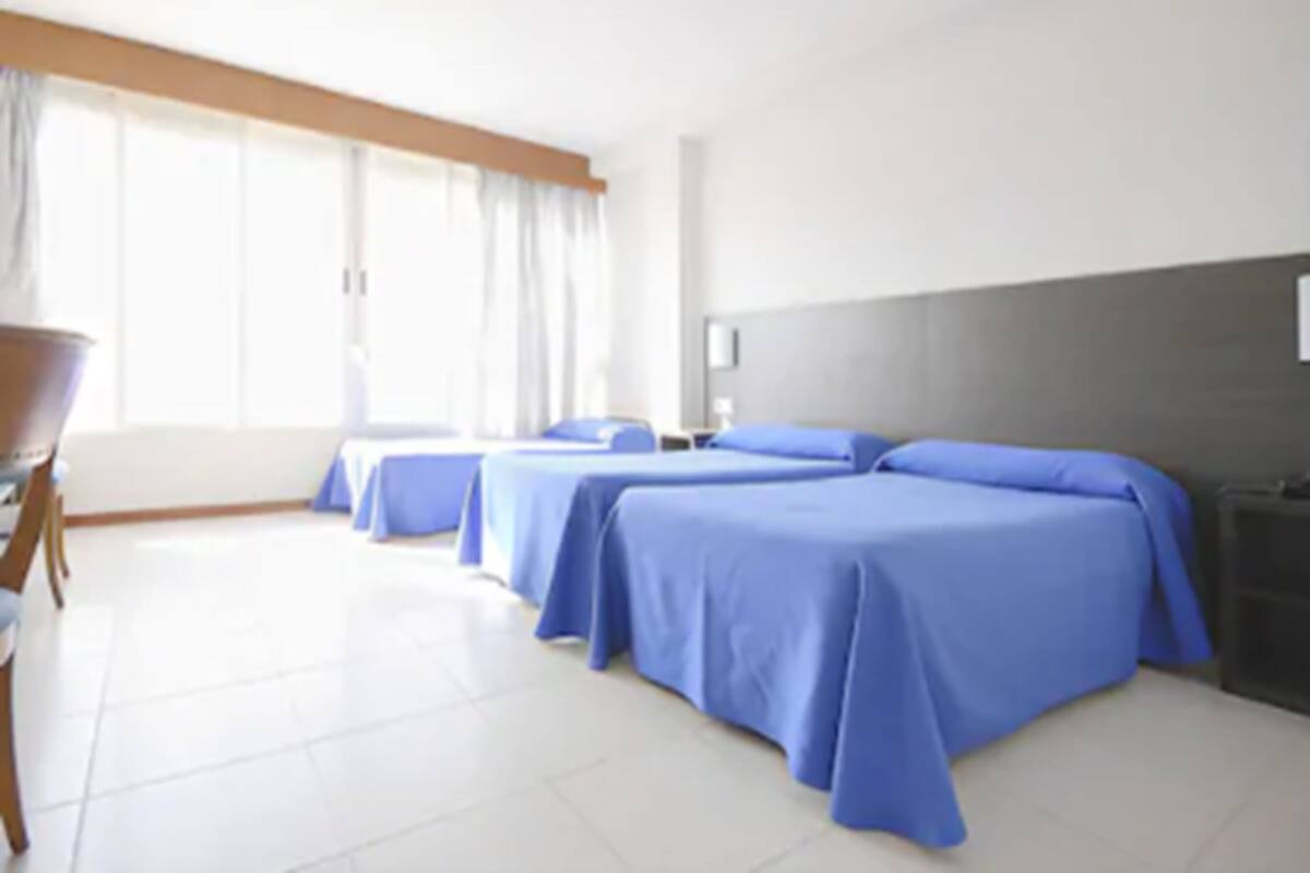 A hotel room with three single beds, a desk, and a chair.