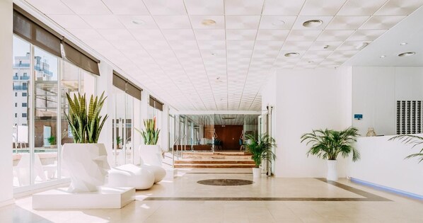 A modern hotel lobby with a spacious layout, large windows, and a reception desk. - Hotel Safari (Gandia)