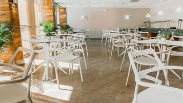 Een moderne eetruimte met witte stoelen en tafels, een houten accentmuur en potplanten.
