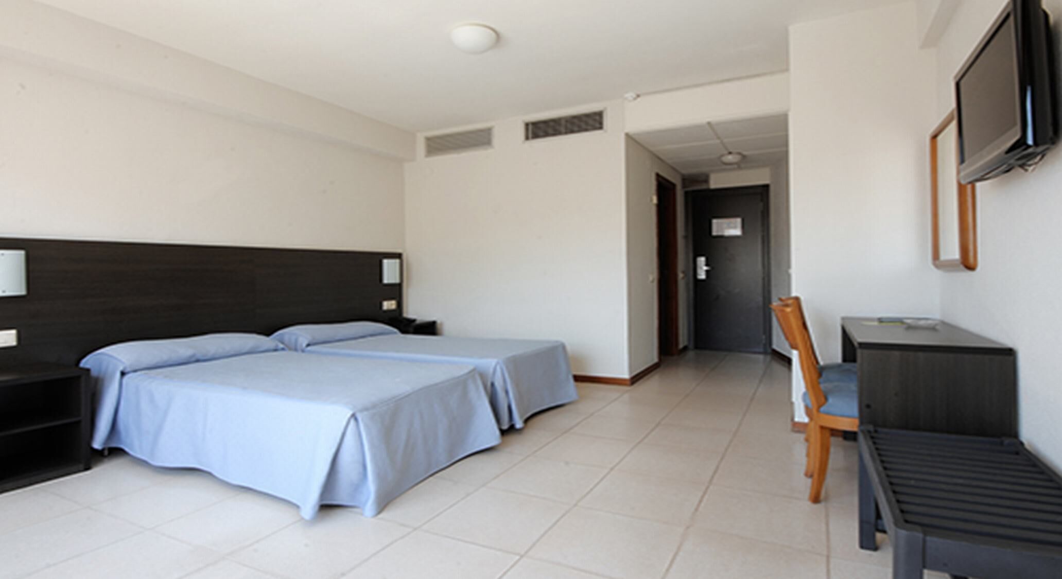 A hotel room with a bed, bedside tables, a desk, a chair, and a television.