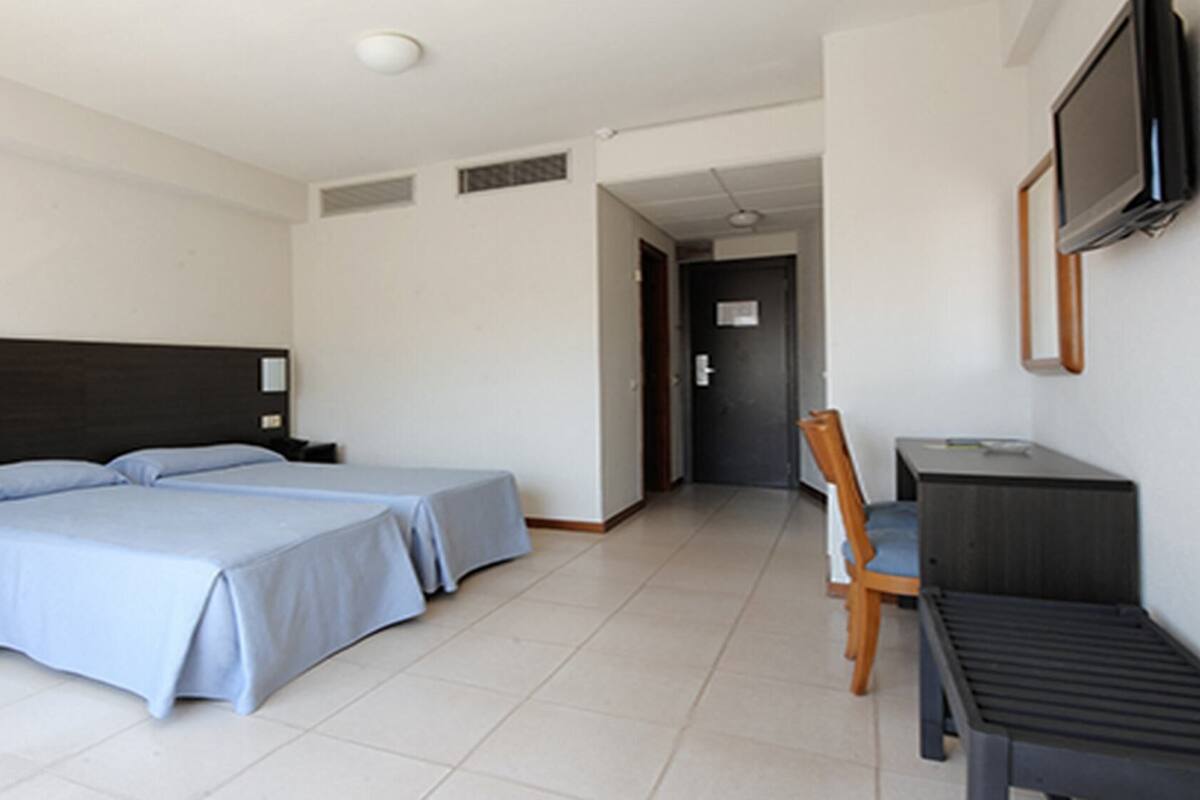 A hotel room with a bed, bedside tables, a desk, a chair, and a television.