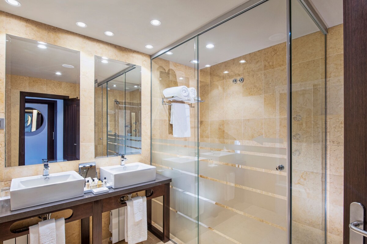 A modern bathroom with a glass-enclosed shower, two sinks, and a large mirror.