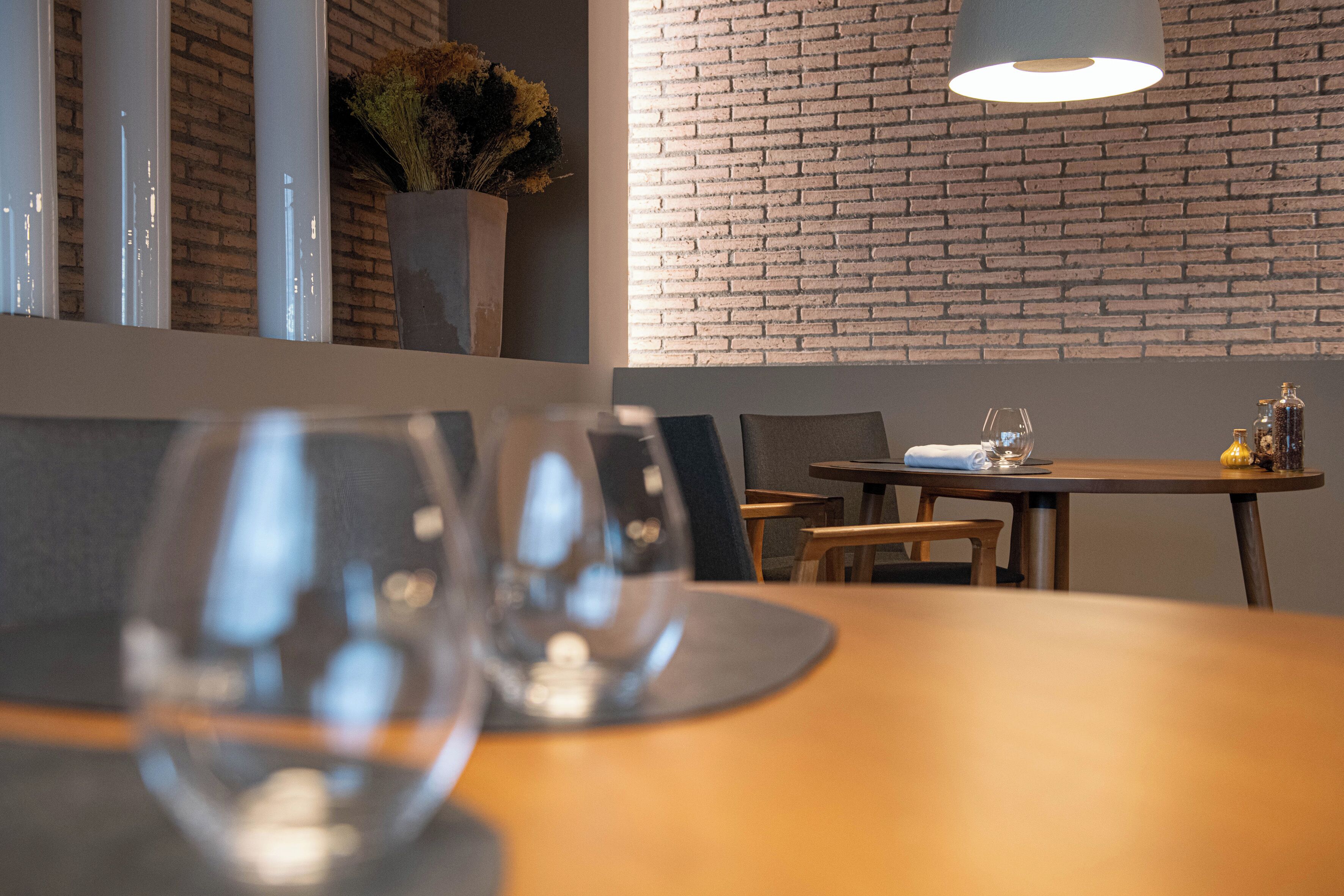 A restaurant interior with a brick wall, wooden tables, and a hanging light fixture.