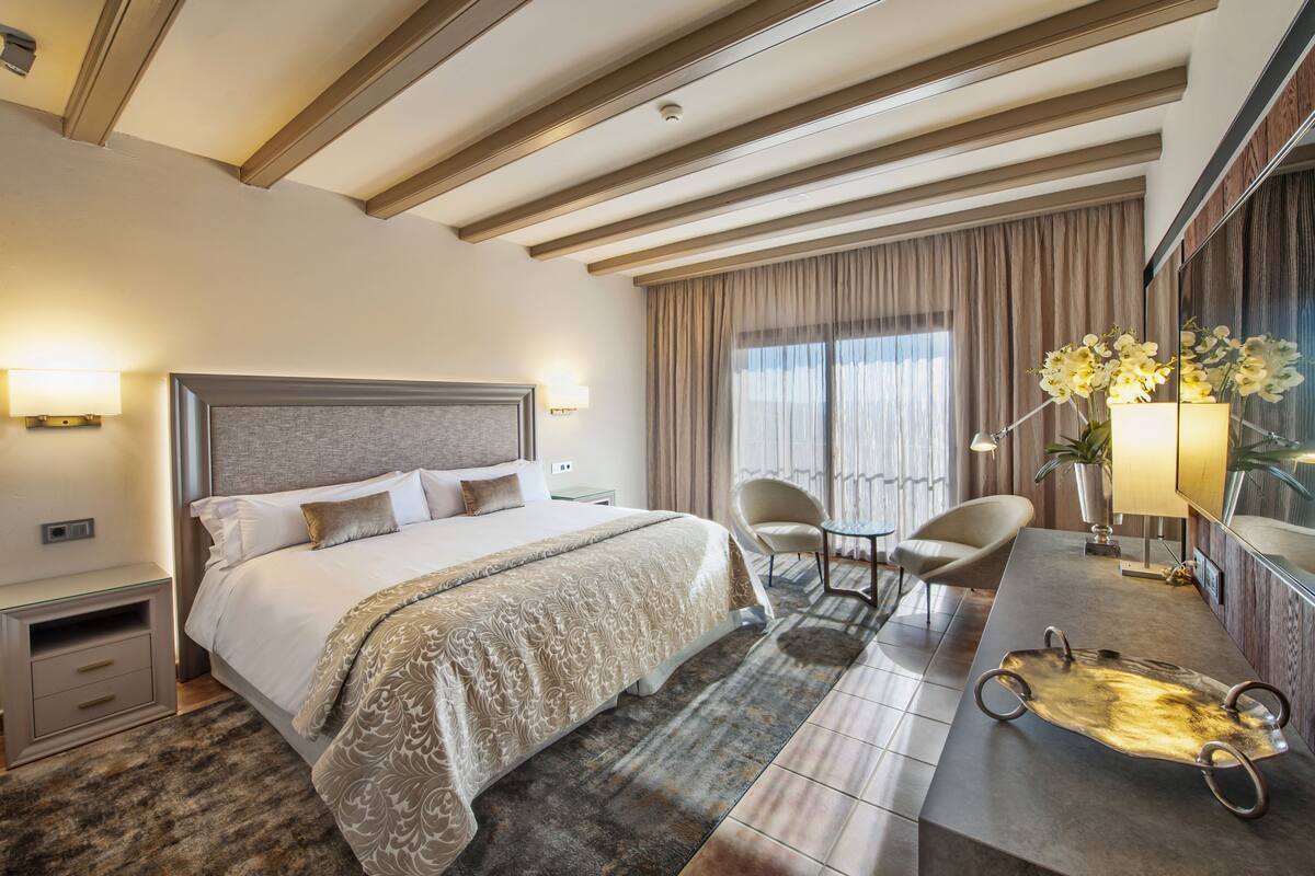 Habitación de hotel con una cama grande, un escritorio, una silla, un espejo y una ventana con cortinas.