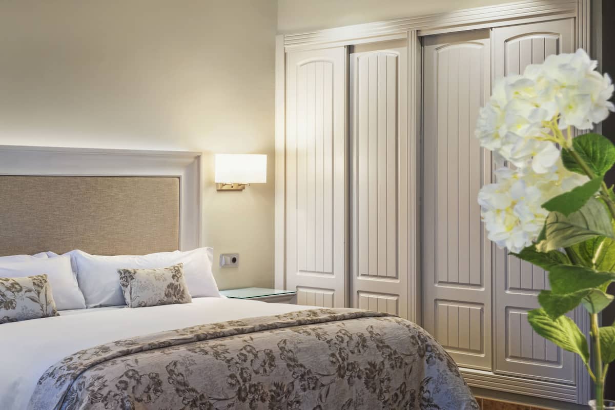 Una habitación de hotel con una cama, una mesita de noche, una lámpara y un armario.