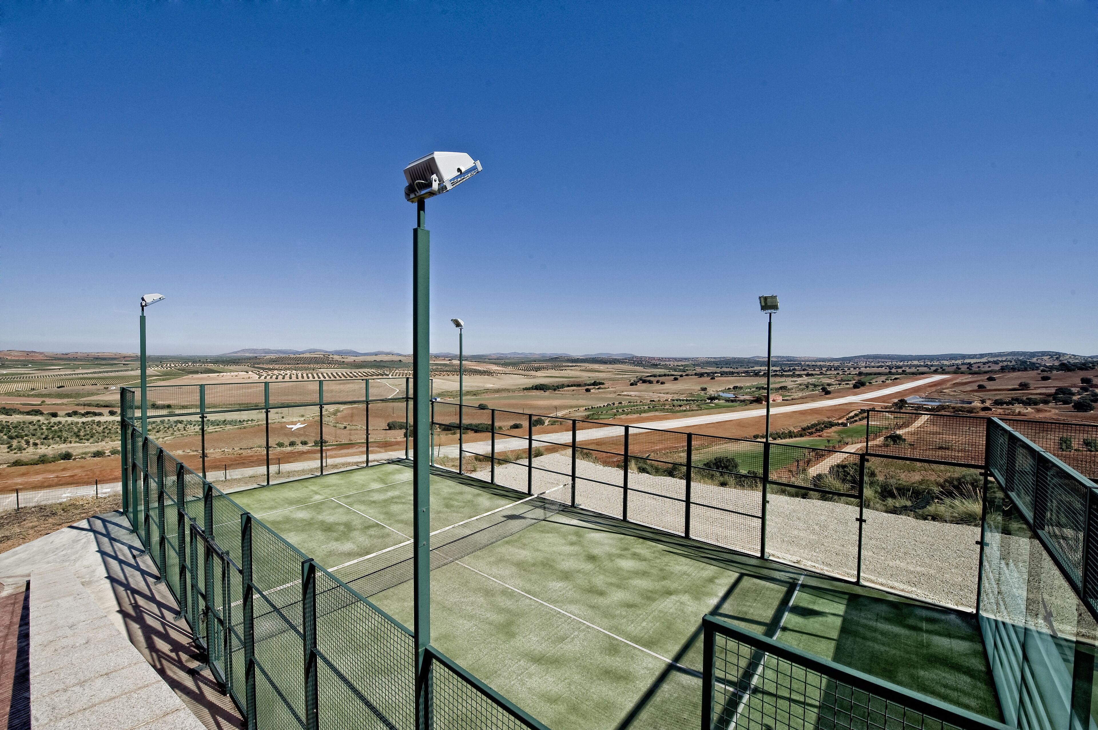 Una cancha de tenis con una valla verde y una vista despejada del paisaje circundante.