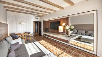A modern living room with a sofa, dining table, chairs, and a large mirror reflecting a bedroom.