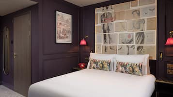 A bedroom with a large bed, a red telephone, and a wall decorated with framed pictures.