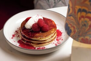 Ein Stapel Pfannkuchen mit Himbeeren und Schlagsahne auf einem Teller.