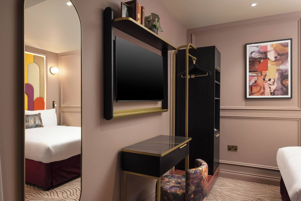 Een hotelkamer met een bed, een bureau, een spiegel, een televisie en een schilderij aan de muur.